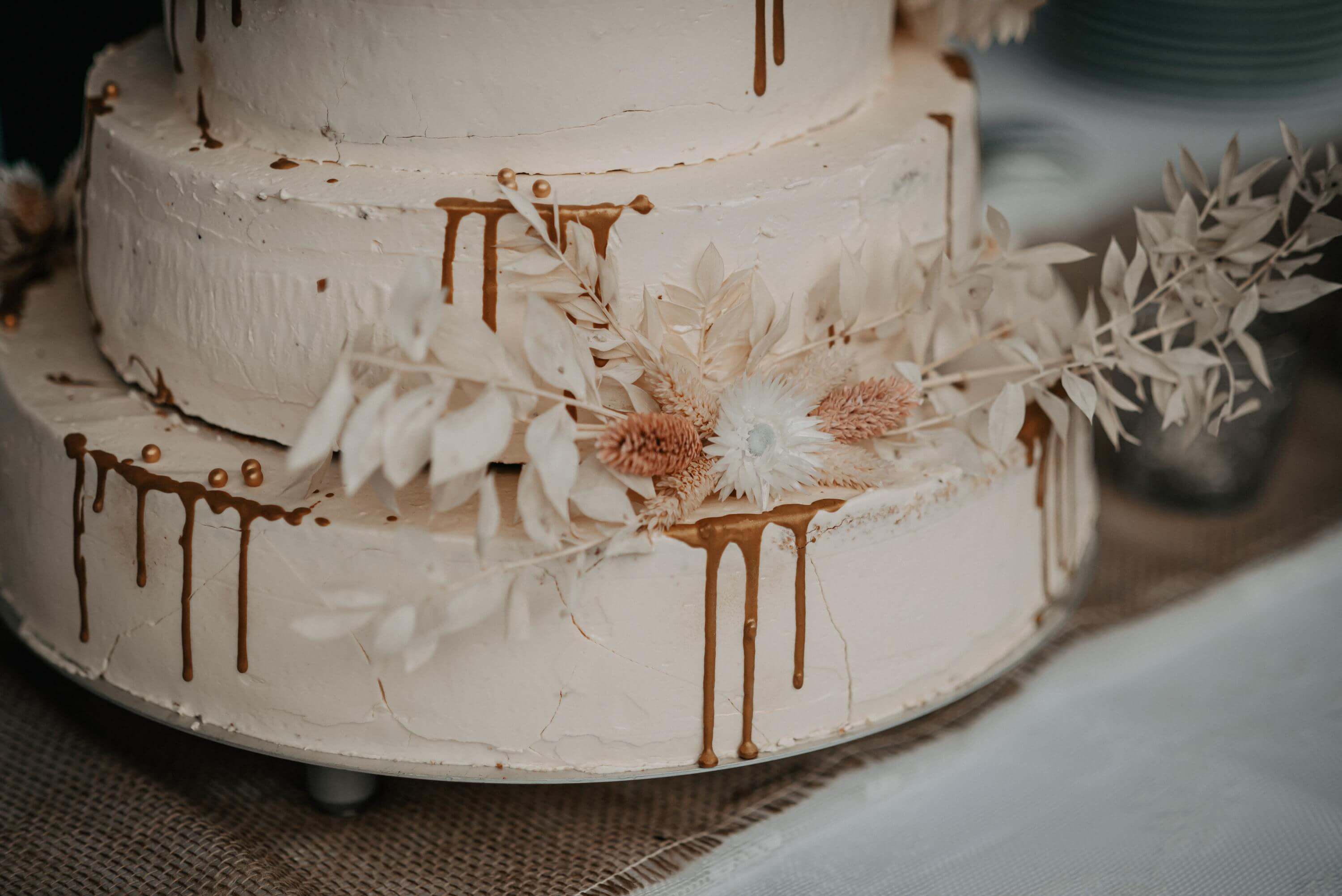 Eine dreigeschössige Buttercréme-Hochzeitstorte ist im Drip Cake Stil dekoriert und steht zum Verzehr bereit.