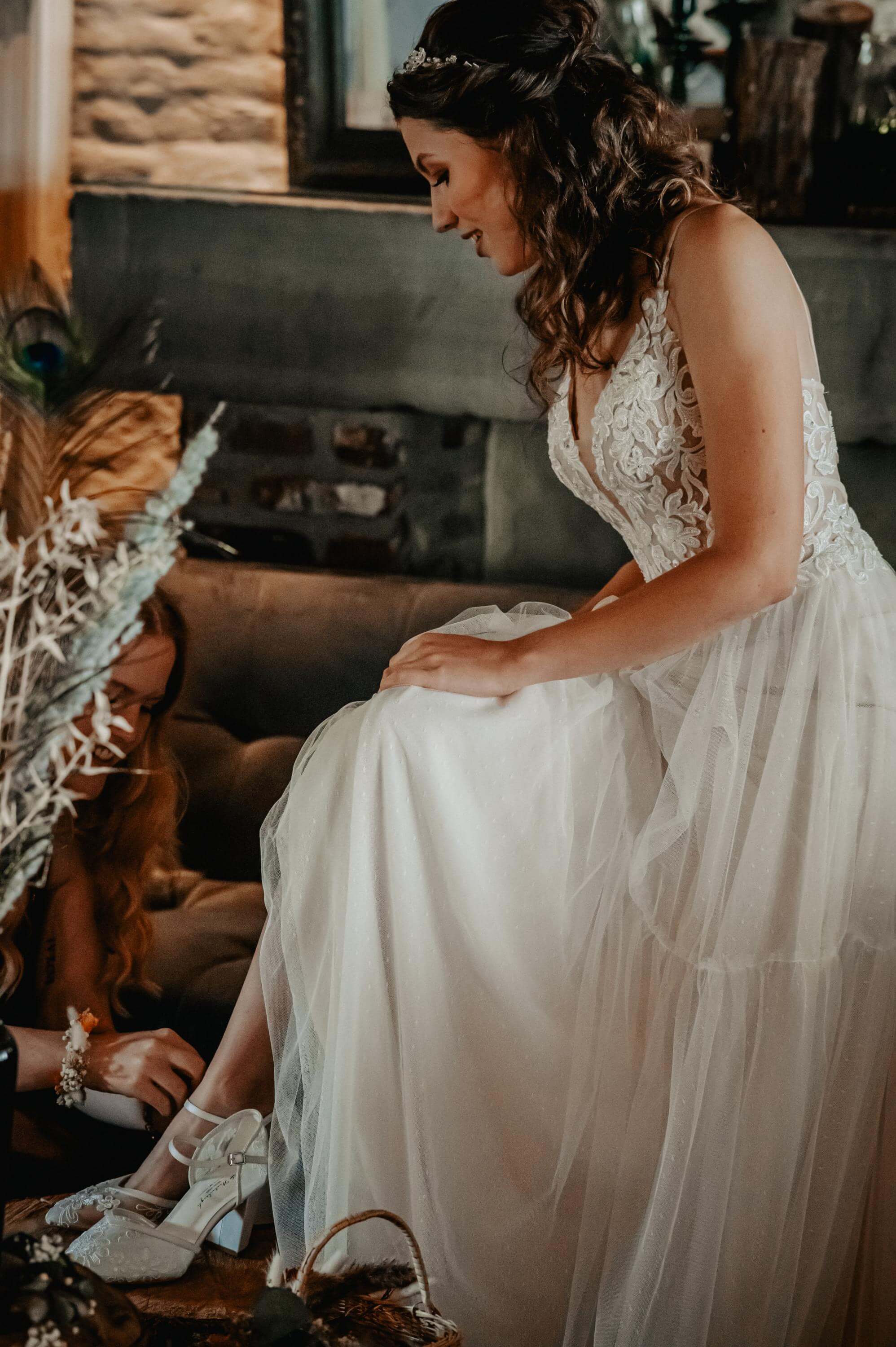 Beim Getting Ready werden der Braut im Hochzeitskleid sitzend die halbhohen offenen Schuhe angezogen.