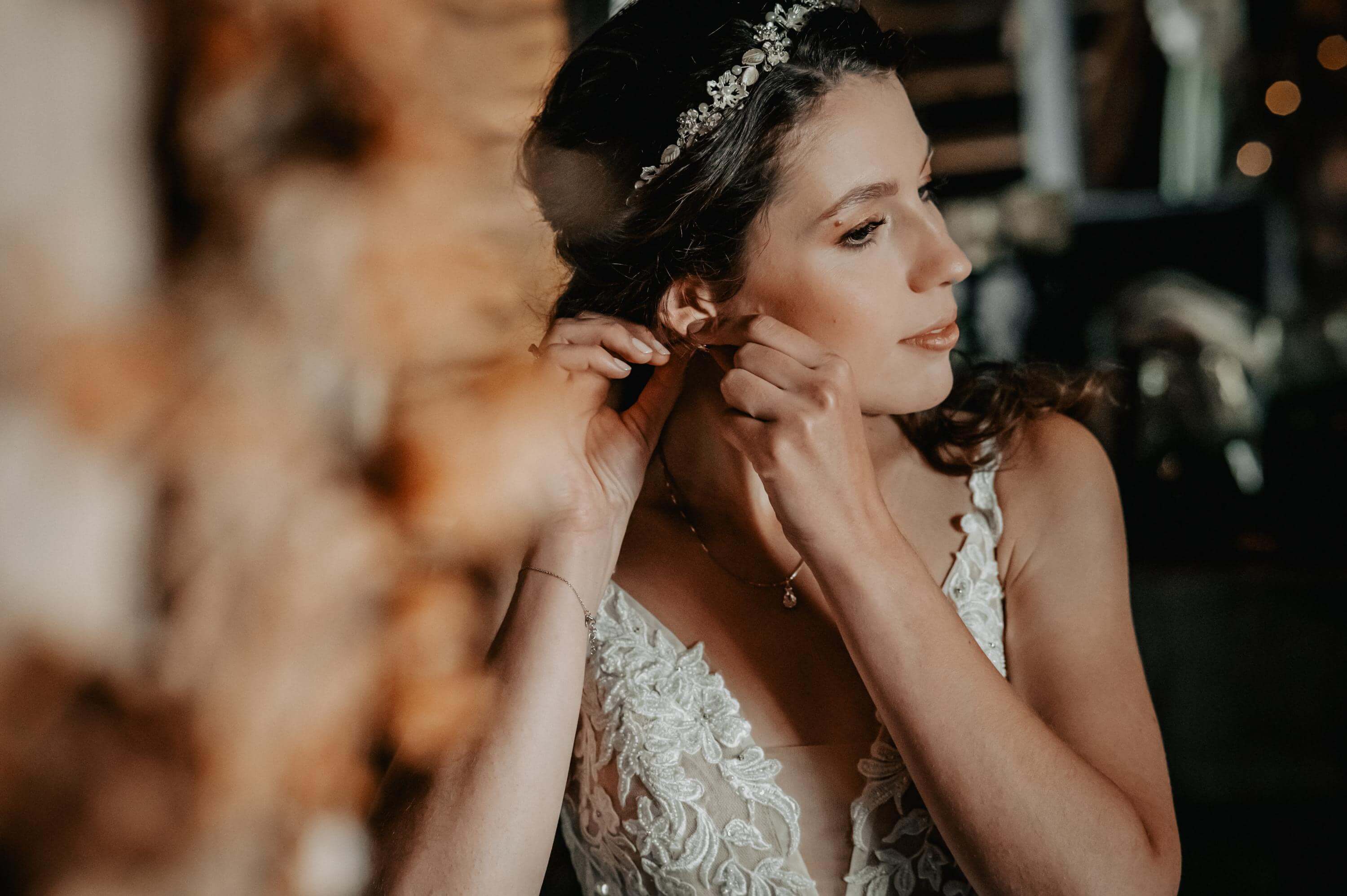 Mit konzentriertem Blick zur Seite in den Spiegel steckt sich die Braut beim Getting Ready einen Ohrring an.