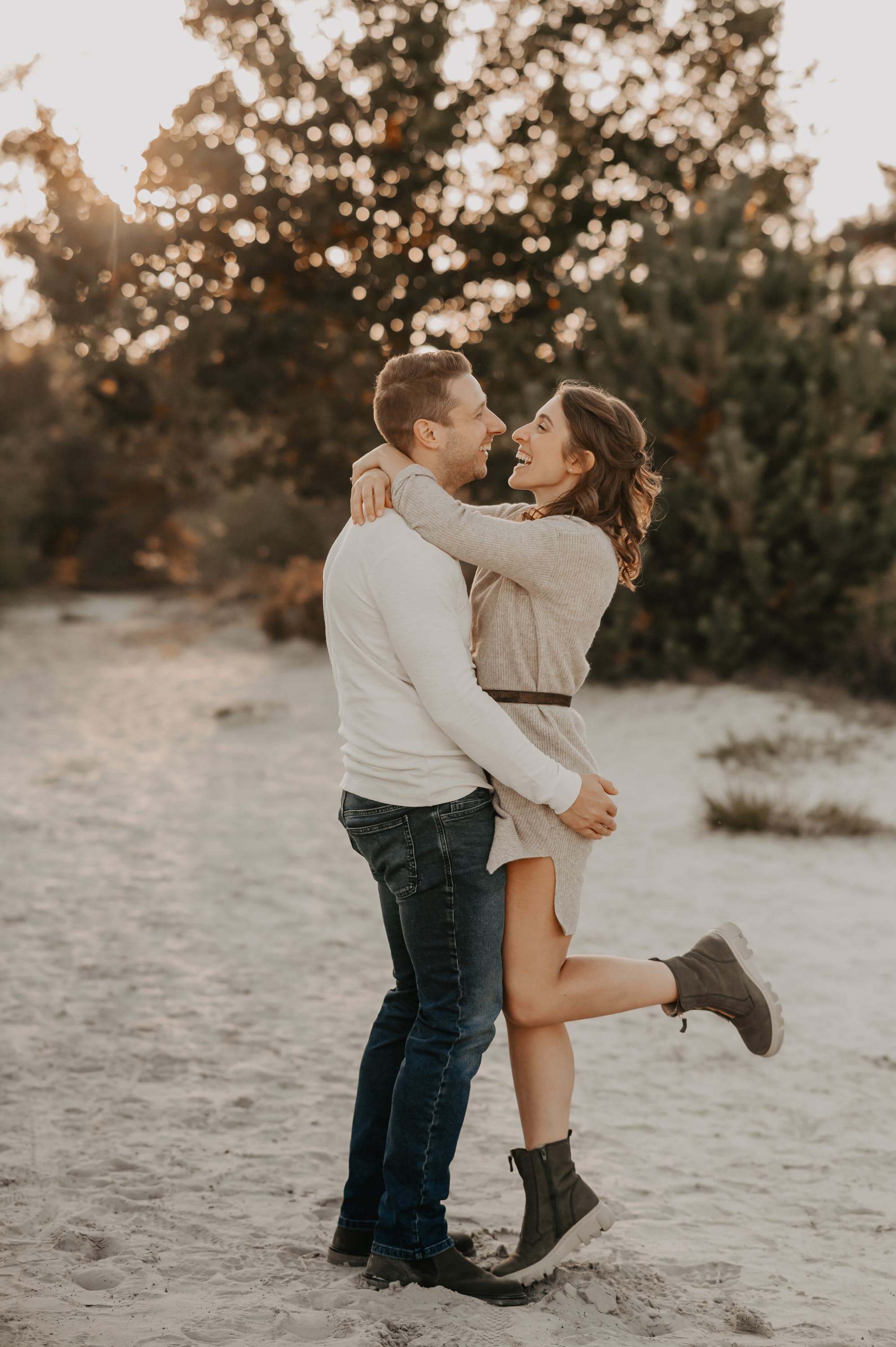 A young couple stands in a tight embrace on the heath sand and both look deep into each other's eyes while she has put her arms around his neck and bends one leg.