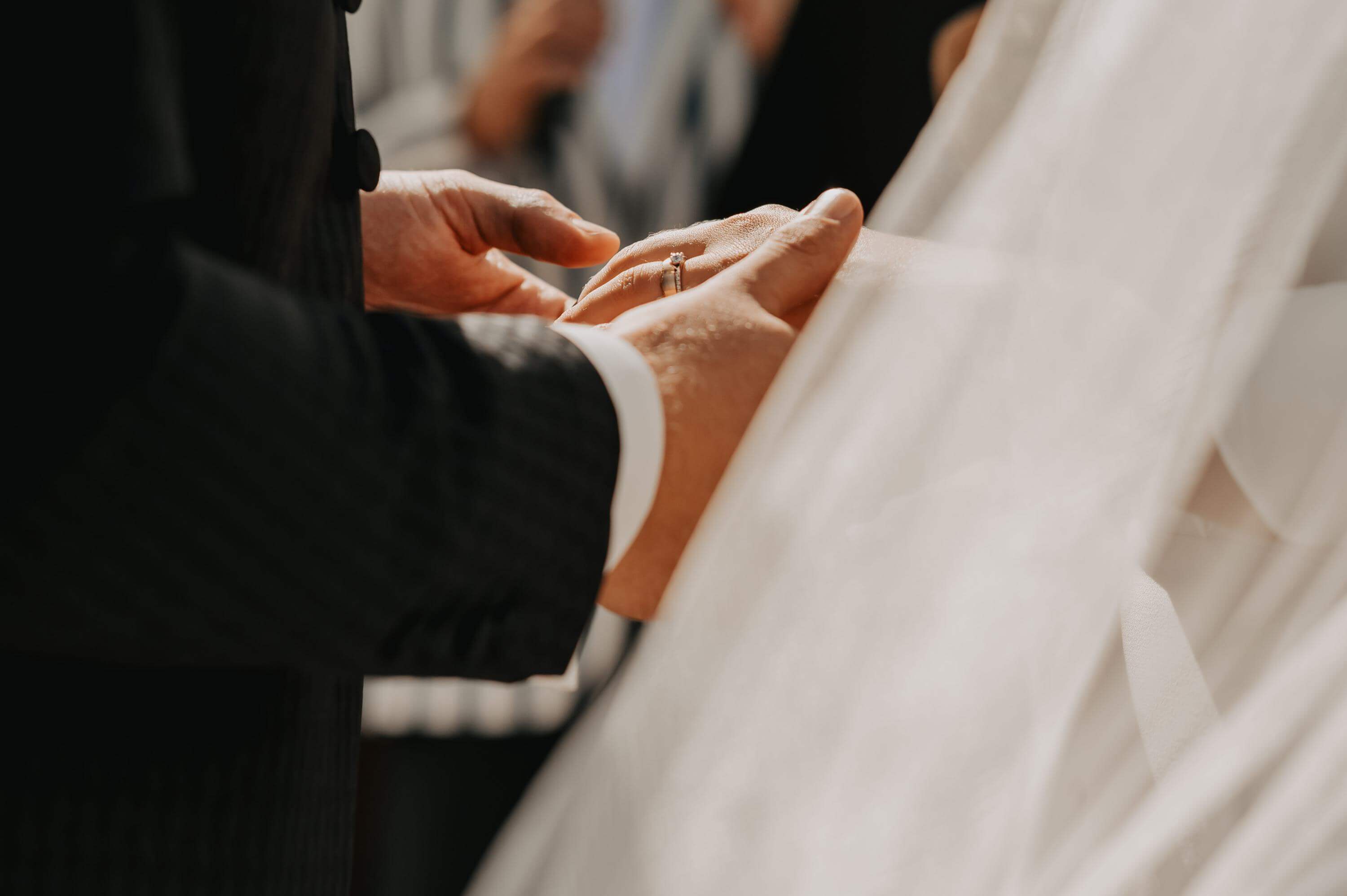 Nahaufnahme der Hand der Braut mit angestecktem Trauring mit Diamanten, die vom Bräutigam selbst gehalten wird.